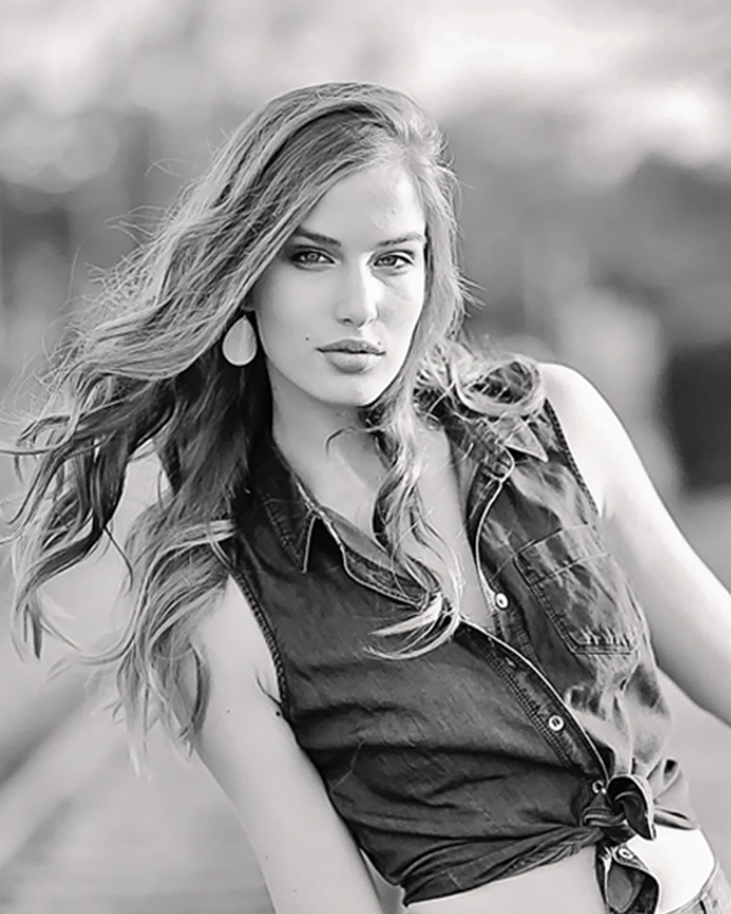 Young woman with flowing hair poses confidently in a sleeveless denim shirt, tied at the waist. The black-and-white photo conveys a strong, classic feel.